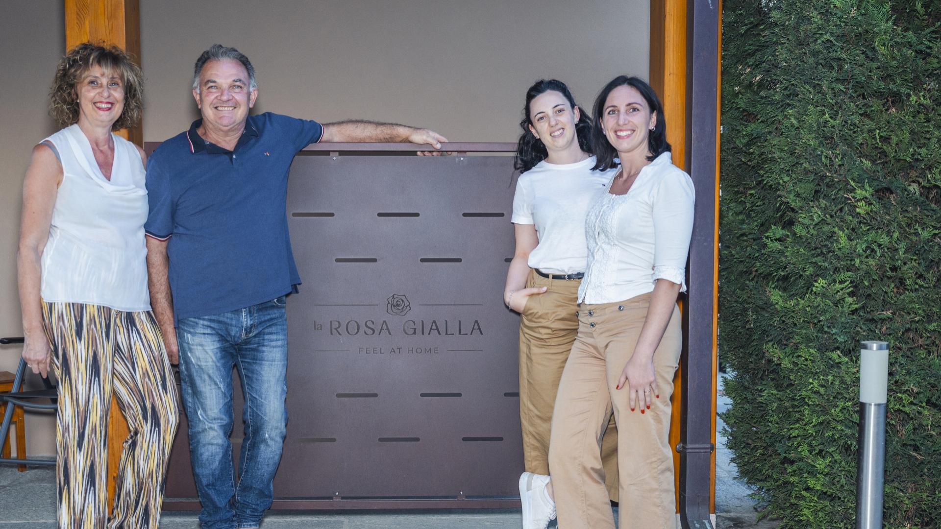 Quattro persone sorridenti davanti al cartello 'la Rosa Gialla'.