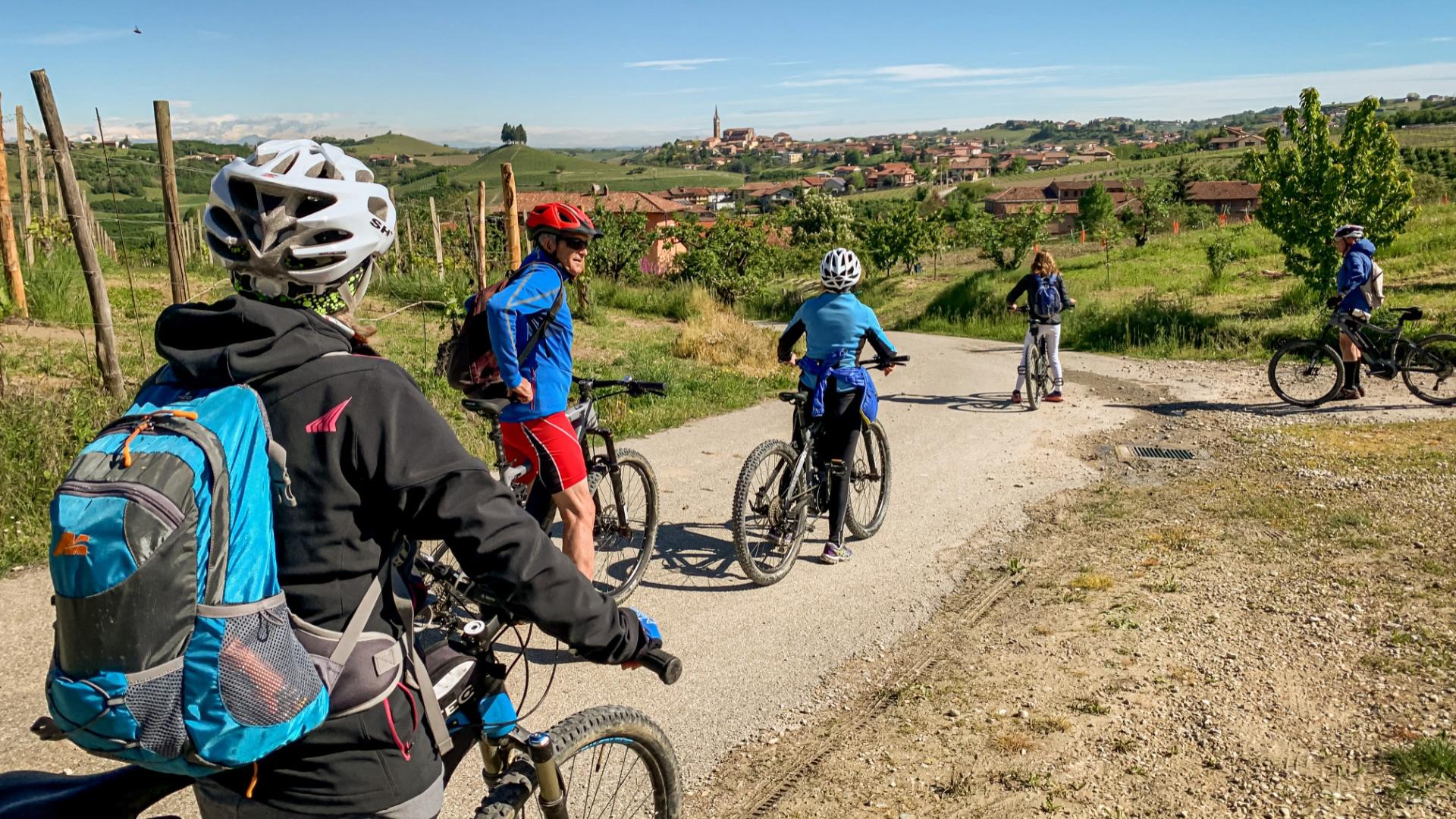 Gruppo di ciclisti su una strada di campagna, con vista su un villaggio collinare.