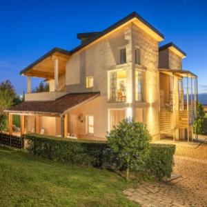 Villa moderna con illuminazione serale, giardino curato e vista panoramica.