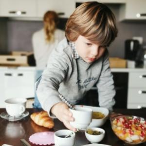Bambino in cucina prepara la colazione con croissant e frutta.