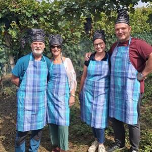 Quattro persone con grembiuli e cappelli da cuoco, sorridono in un vigneto.