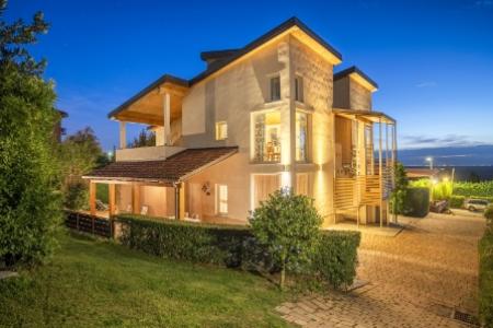Villa moderna illuminata di notte, con giardino curato e vista panoramica.