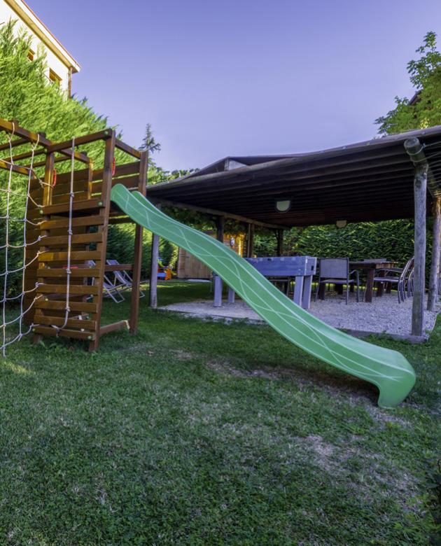 Giardino con scivolo verde e area coperta con tavoli e calcetto.
