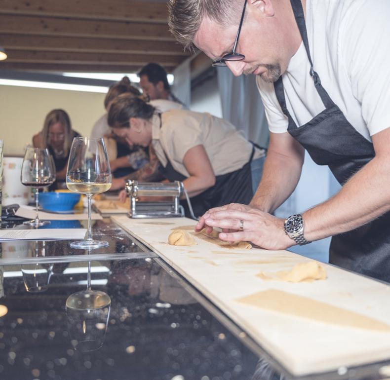 People making fresh pasta in a cooking class with wine.